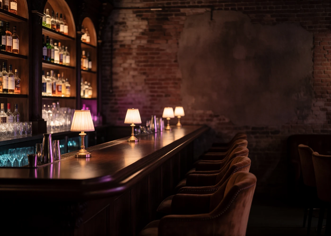 Empty refined Midwestern cocktail bar interior at night with a long walnut bar and low velvet armchairs